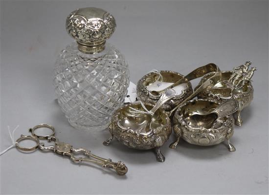 A set of four embossed silver bun salts, a silver-mounted hobnail-cut glass toilet bottle, silver caddy spoons, etc.,